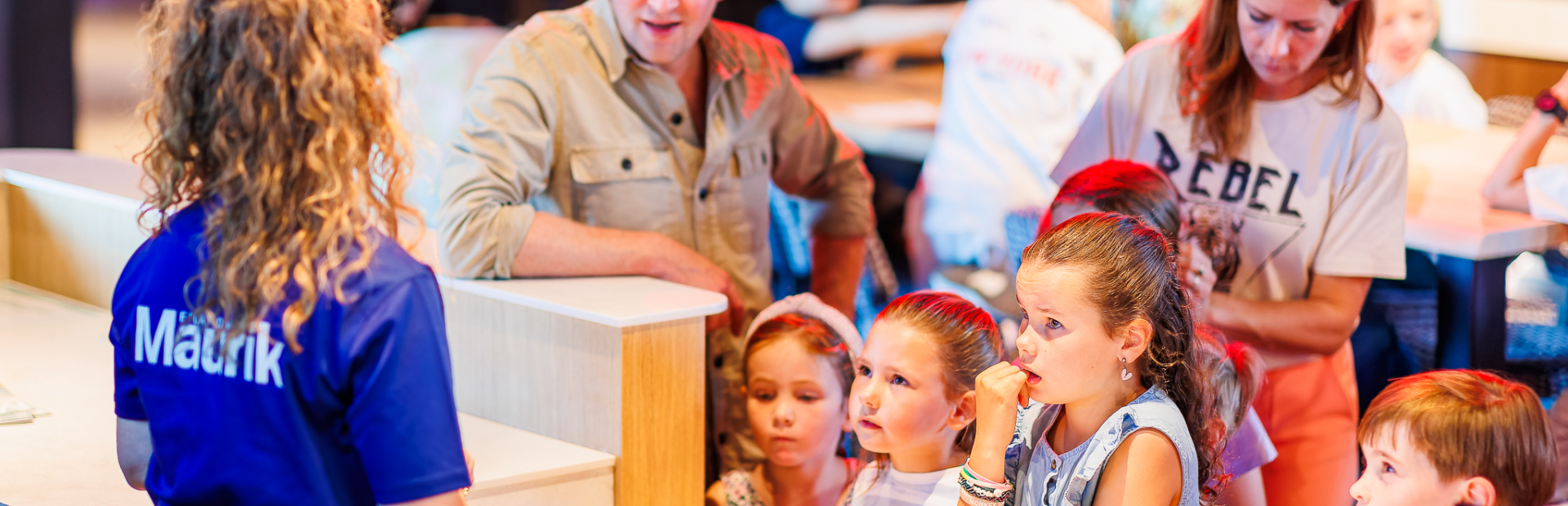 Een medewerker legt de activiteit sjoelen uit aan een gezin met kinderen