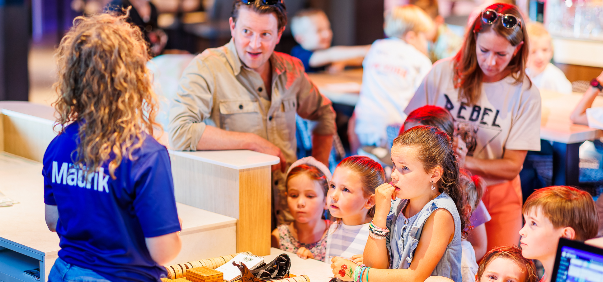 Een medewerker legt de activiteit sjoelen uit aan een gezin met kinderen