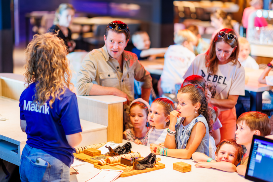 Een medewerker legt de activiteit sjoelen uit aan een gezin met kinderen