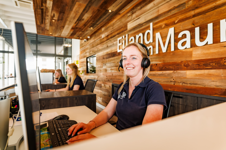 Een receptionisten die met een lach een gast helpen met hun reservering