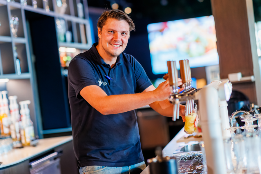 Een horeca medewerker die een bier tapt aan de bar